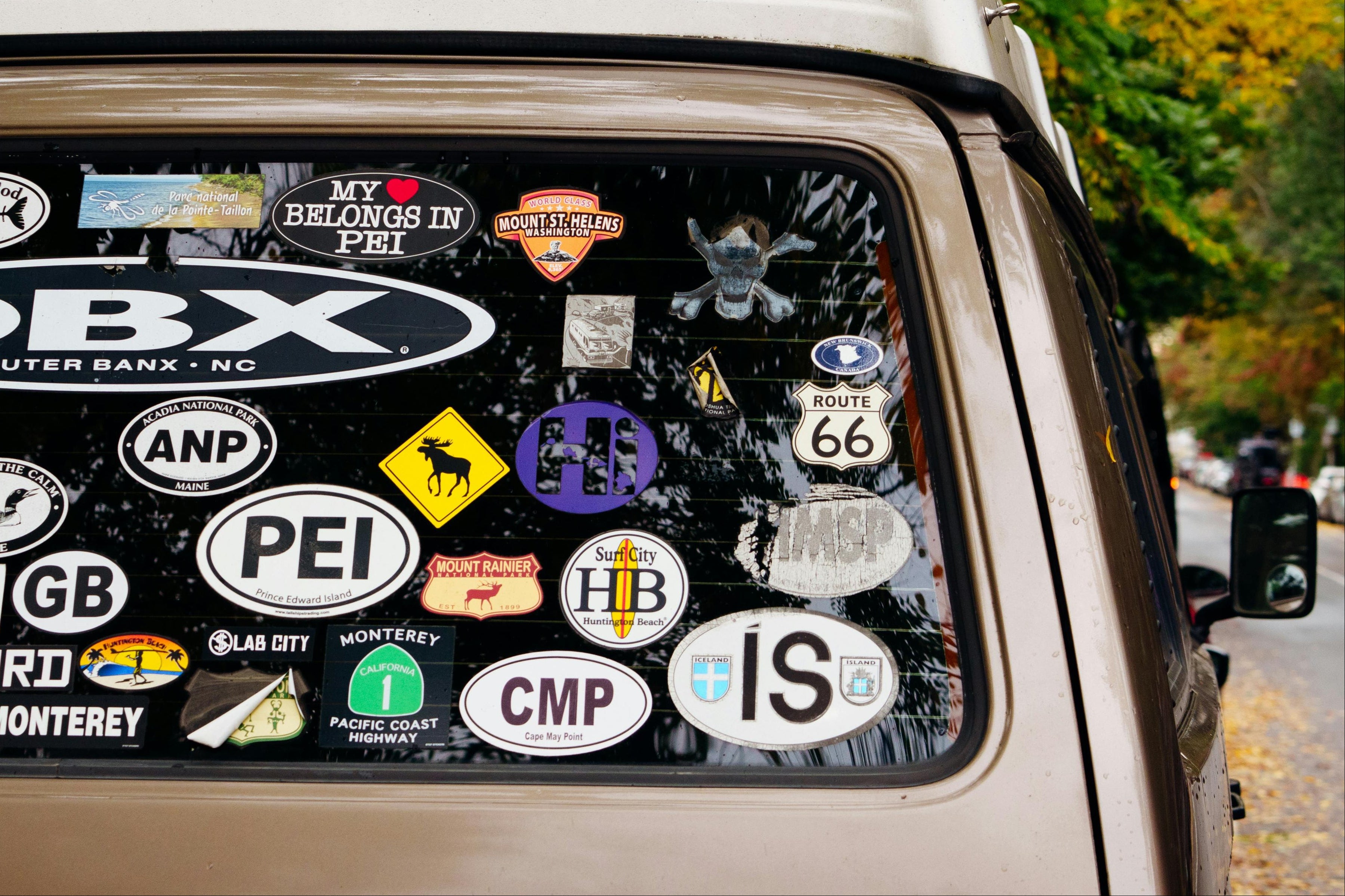 Car window with various stickers, including a prominent 'OBX' sticker, on a blurred outdoor background.